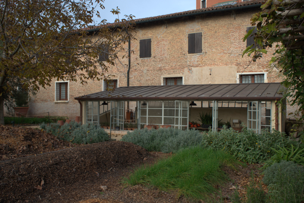 The greenhouse and garden area of the convent set against a traditional brick building with shuttered windows, surrounded by herbs and greenery. This peaceful space is part of the Convent Garden of the Church of the Most Holy Redeemer.