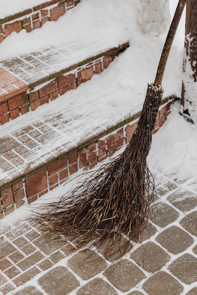 Traditional broom resting on snowy brick steps during winter.