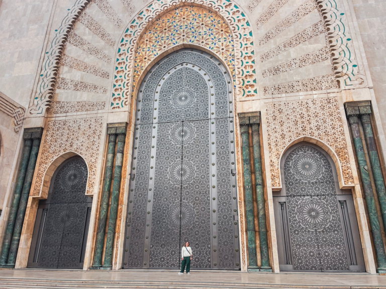 woman standing in front of Hassain II Mosque in Casablanca in front of a grand door with zelige around it