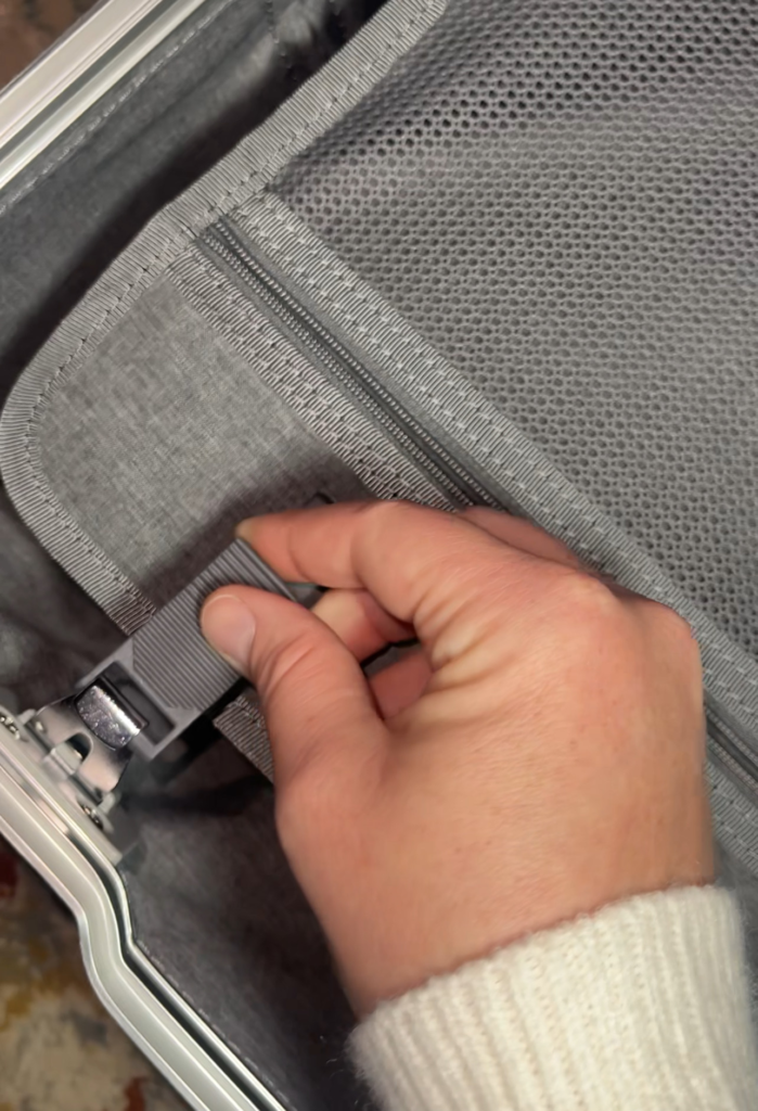 Top-down view of a hand securing the adjustable strap inside the Level8 Gibraltar carry-on, with visible zippered mesh pocket and reinforced seam detailing.