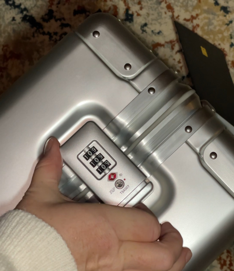 Close-up of the TSA-approved combination lock on the Level8 Luminous 20-inch carry-on in olive green, with zipper pulls secured in place. The lock is set to 000 and shows the Travel Sentry red diamond symbol.