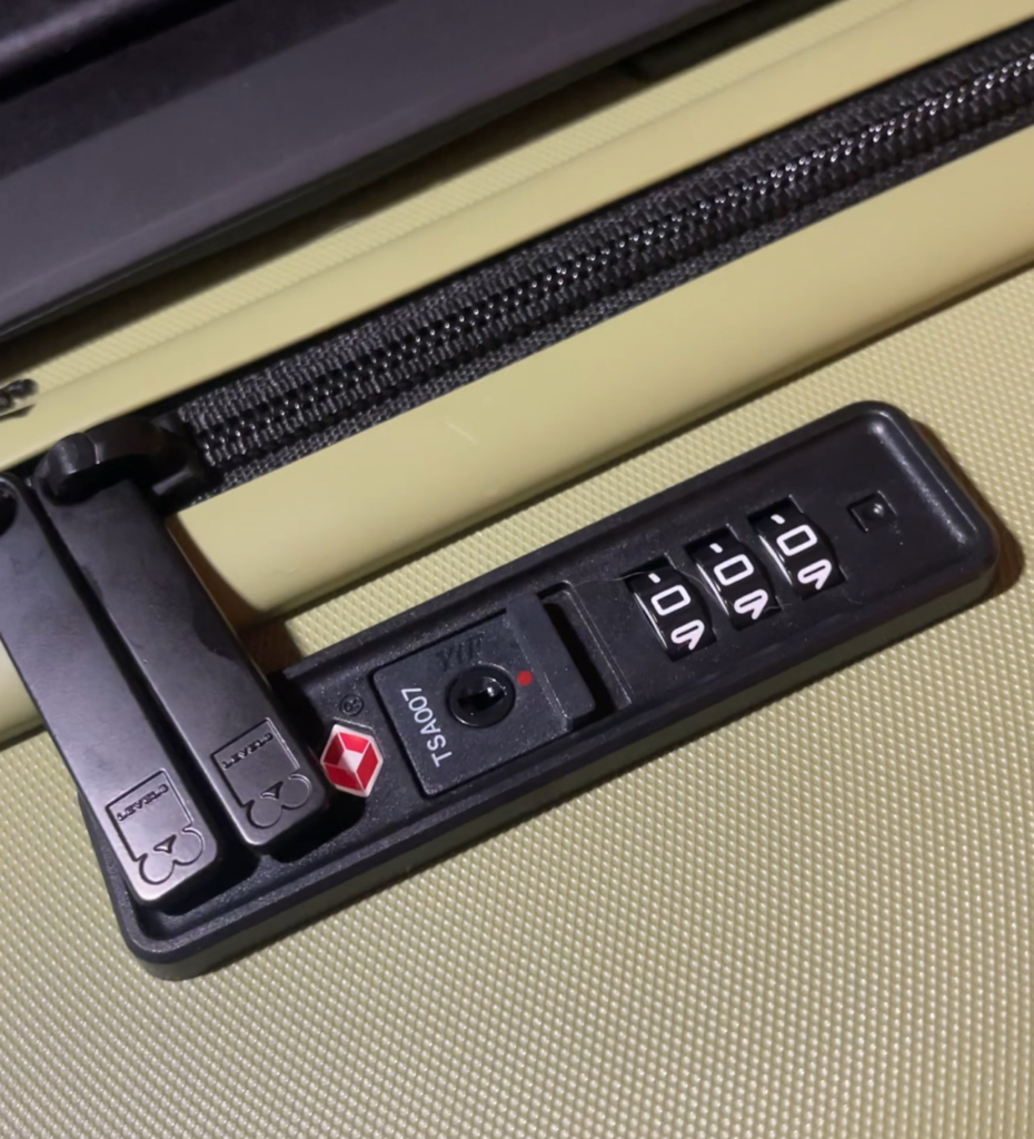 Close-up of the TSA-approved combination lock on the Level8 Luminous 20-inch carry-on in olive green, with zipper pulls secured in place. The lock is set to 000 and shows the Travel Sentry red diamond symbol.