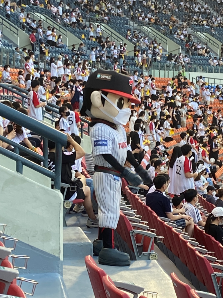 A costumed baseball team mascot in an LG Twins uniform stands among fans at a crowded stadium, engaging with the audience during a game in Seoul. Attending a baseball game is a lively and popular thing to do in Seoul South Korea.