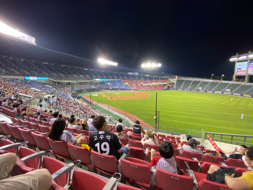 View from the stands at a nighttime baseball game in Seoul, with fans wearing team jerseys and a well-lit field in the distance. Watching a game at this vibrant stadium is a fun and energetic thing to do in Seoul South Korea.
