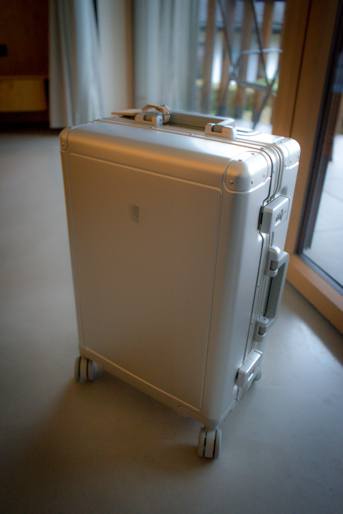 Sleek silver Level 8 Gibraltar Aluminum Carry-On 20" standing upright on four spinner wheels in a modern room with soft lighting. The hard-shell suitcase features reinforced corners, a TSA-approved lock, and a smooth matte finish.