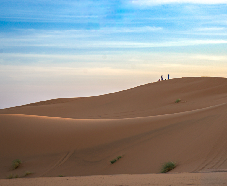 two sillhouettes in the desert landscape of Merzouga in Morocco against a blue sky