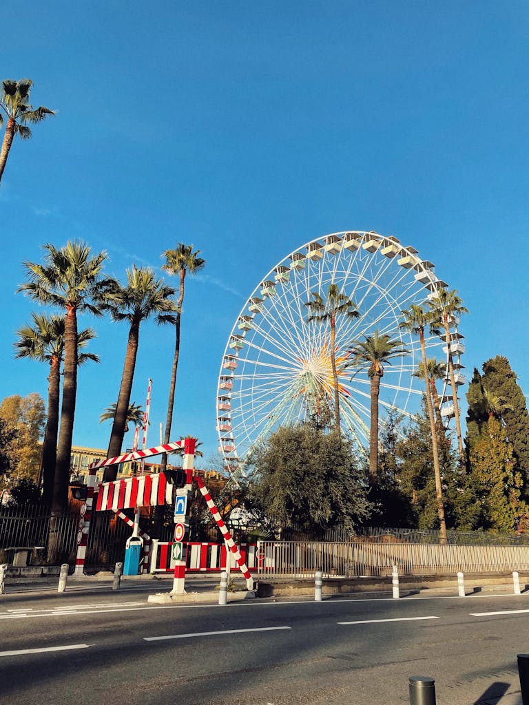 Colorful ferris wheel at an amusement park in Nice, France, under a clear blue sky with palm trees.