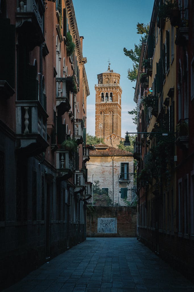 Explore a quiet, narrow street in Venice, showcasing stunning historic architecture and a towering landmark.