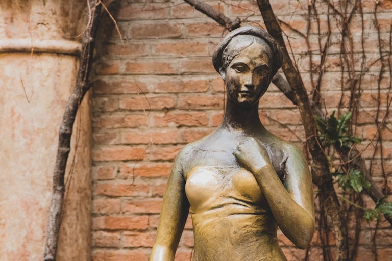 Historic bronze statue of Juliet in Verona, surrounded by rustic brick walls.