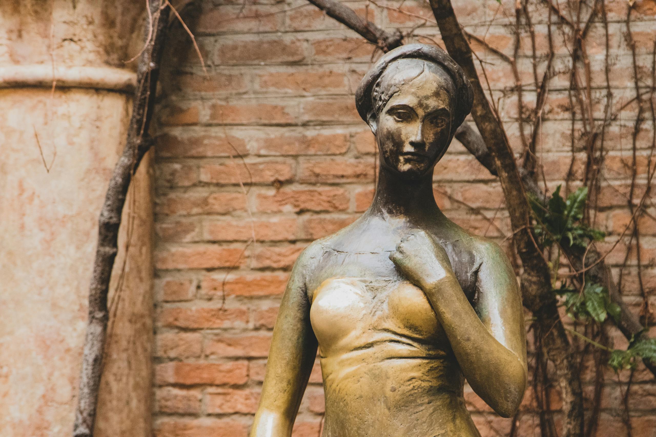 Historic bronze statue of Juliet in Verona, surrounded by rustic brick walls.