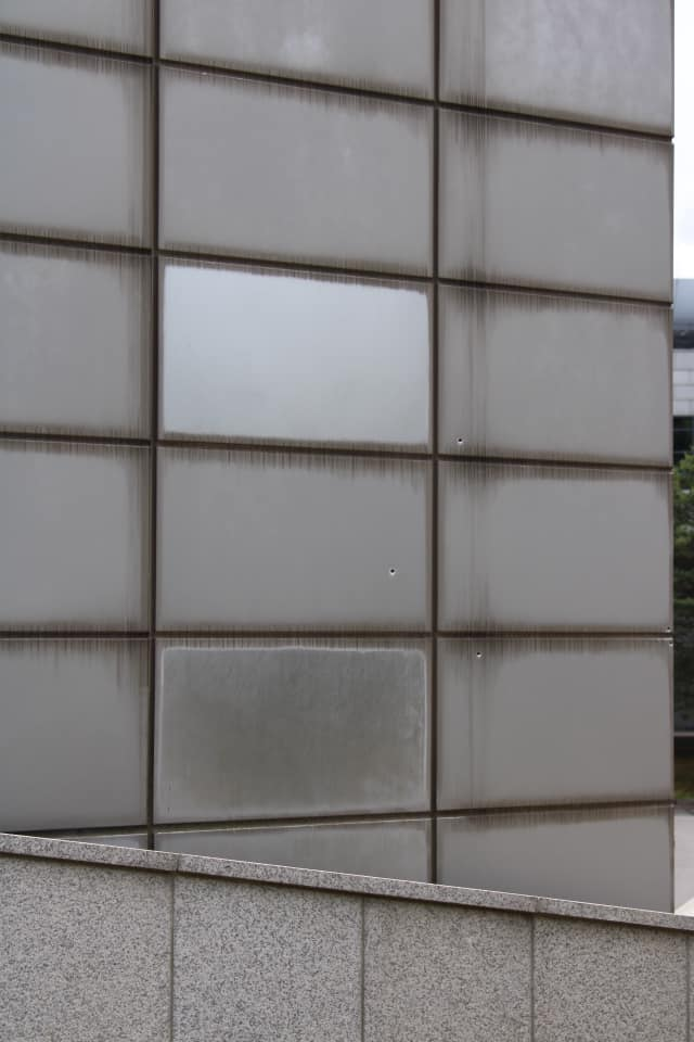 Close view of a modern building wall marked with small bullet holes preserved as evidence of past conflict at the DMZ.