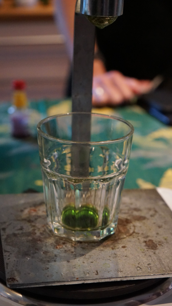 Close up of green cannabis infused liquid dripping into a small glass on a metal scale during a hands on workshop. The focus highlights the careful measuring process used at Get Baked Amsterdam in Amsterdam Netherlands.