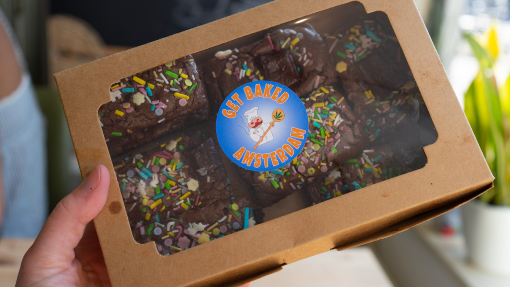 A box of chocolate brownies topped with colorful sprinkles labeled Get Baked Amsterdam. The packaging displays the playful logo and finished cannabis infused brownies made during the workshop in Amsterdam Netherlands.