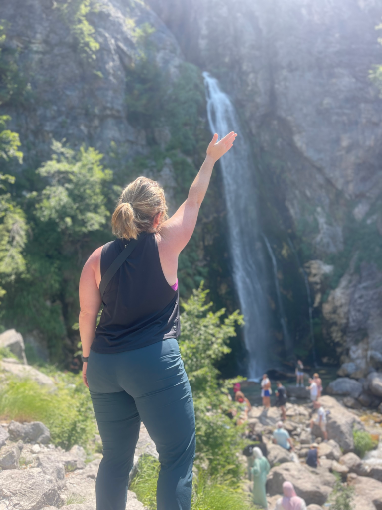 woman with her arm up standing in front of Grunas Waterfall in Theth Albania