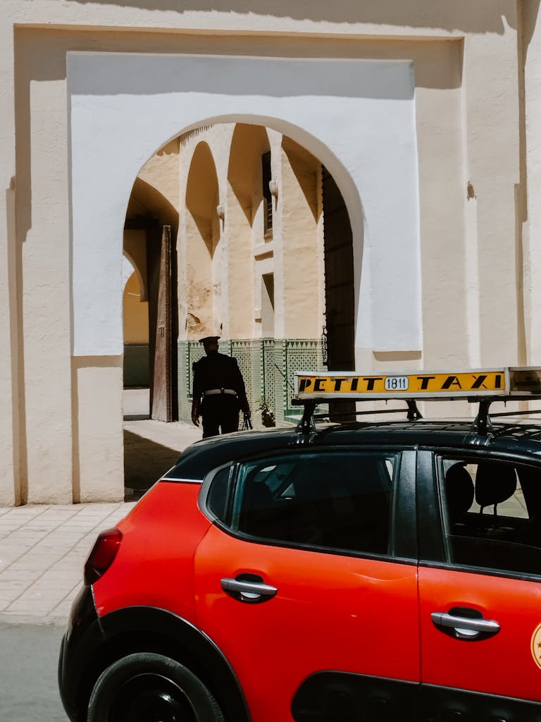 Explore the vibrant streets of Fes Medina with a striking red taxi against historic architecture.