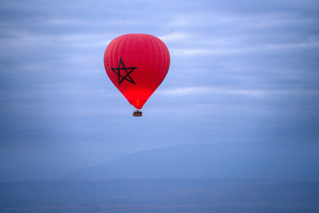 Bright red hot air balloon with a green star drifting over misty landscapes near Marrakech, capturing the peaceful experience of a hot air balloon ride.