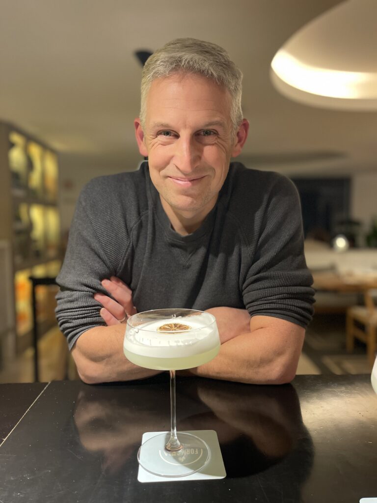 Man sitting at a bar inside Memmo Baleeira in Sagres holding a cocktail with a foamy top, illustrating the relaxed evening atmosphere featured in this Memmo Baleeira review.