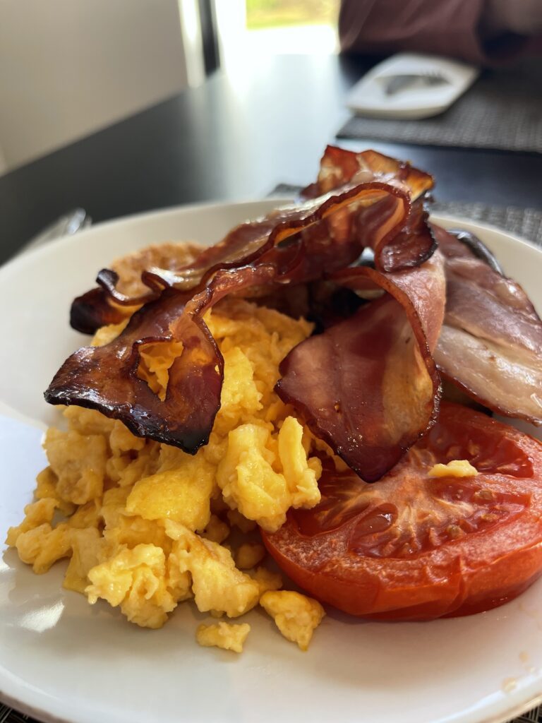 Plate of scrambled eggs with crispy bacon and grilled tomato served at Memmo Baleeira hotel in Sagres, part of the breakfast experience covered in this hotel in the Algarve review.