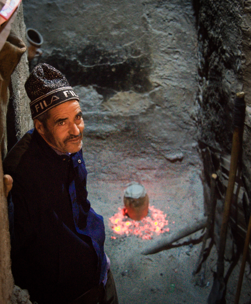 Man leaning against a wall in a narrow Marrakech alley near glowing embers on the ground, capturing a quiet moment in the medina away from the busy souks.