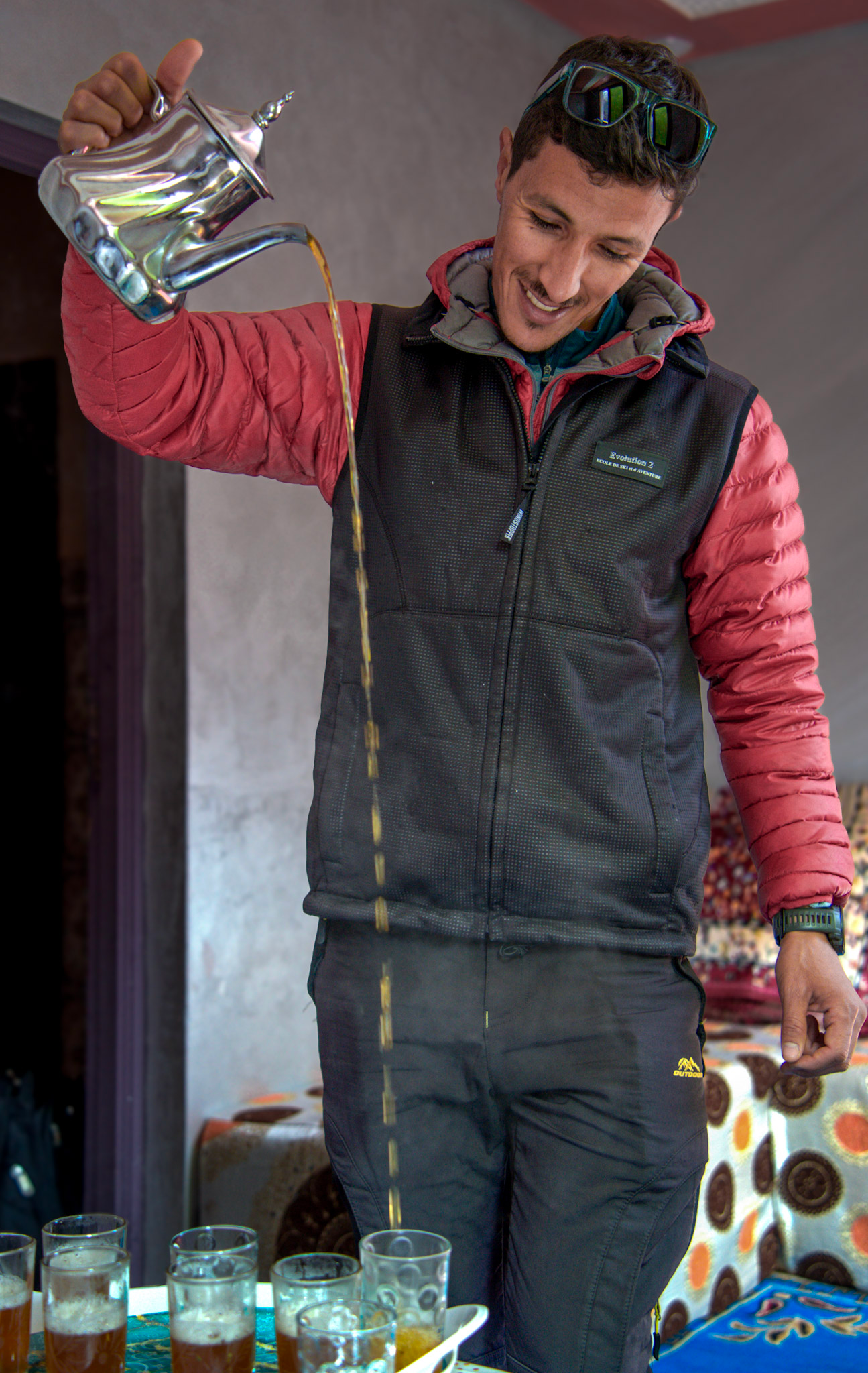 Local guide pours Moroccan mint tea from a silver teapot into small glasses, a traditional moment shared during lunch with a Berber family in the Atlas Mountains.