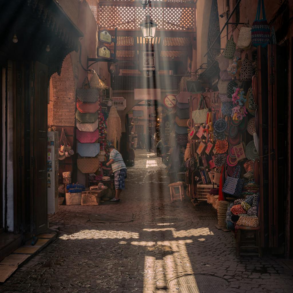 Charming alleyway in Marrakech with sunrays highlighting colorful market stalls.