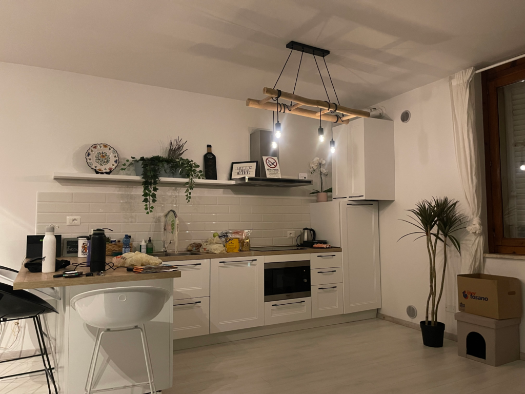 Bright modern kitchen in a Siena apartment with white cabinets wooden countertop and hanging lights above a small dining area. This cozy setup is typical of accommodation you might book during a 2 days in Siena itinerary.