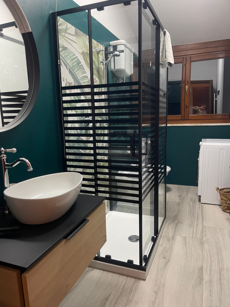 Modern bathroom with glass shower black frame details and a round sink set against green walls and wooden accents. The stylish design adds comfort to a Siena apartment stay.
