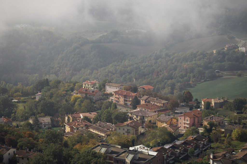 A cluster of pastel houses with terracotta roofs sits on a hillside overlooking misty valleys, showing the peaceful countryside views during 2 days in San Marino.