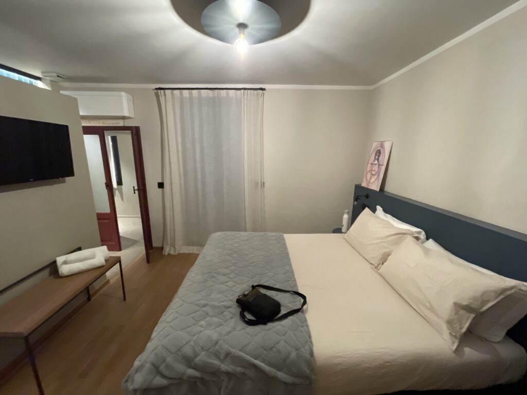 Spacious bedroom at Casa Cicetta featuring a large bed, wall mounted TV, wooden bench, and soft curtains creating a comfortable base for 2 days in San Marino.