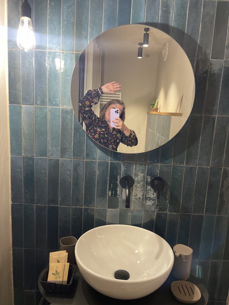 Bathroom at Casa Cicetta with deep green tiled wall, round mirror, and white basin sink as a guest takes a mirror selfie during their 2 days in San Marino stay.