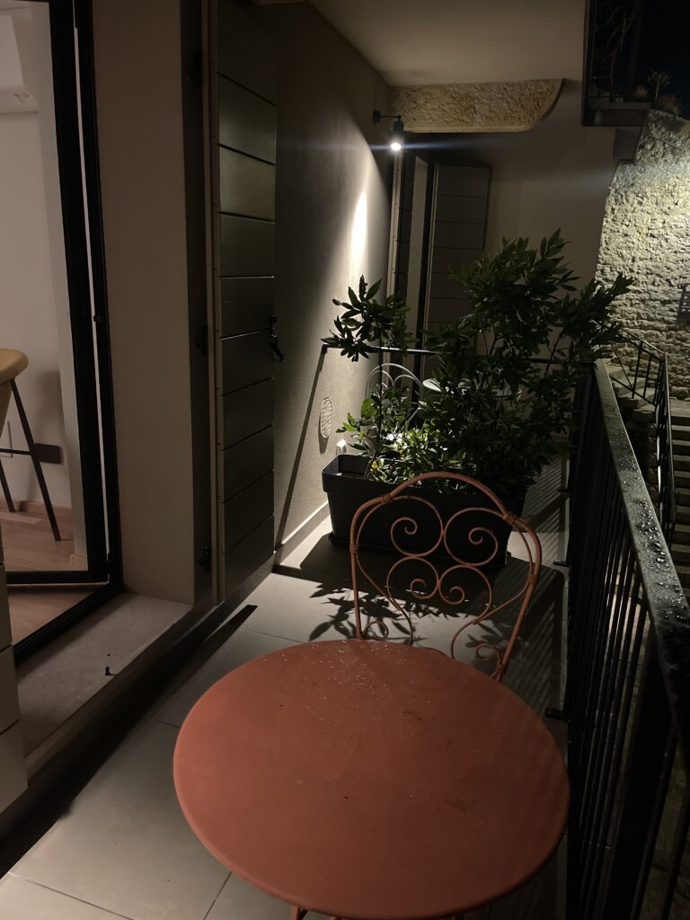 Small private balcony at Casa Cicetta with a round table, chair, and potted plants lit at night, a quiet spot to relax during 2 days in San Marino.