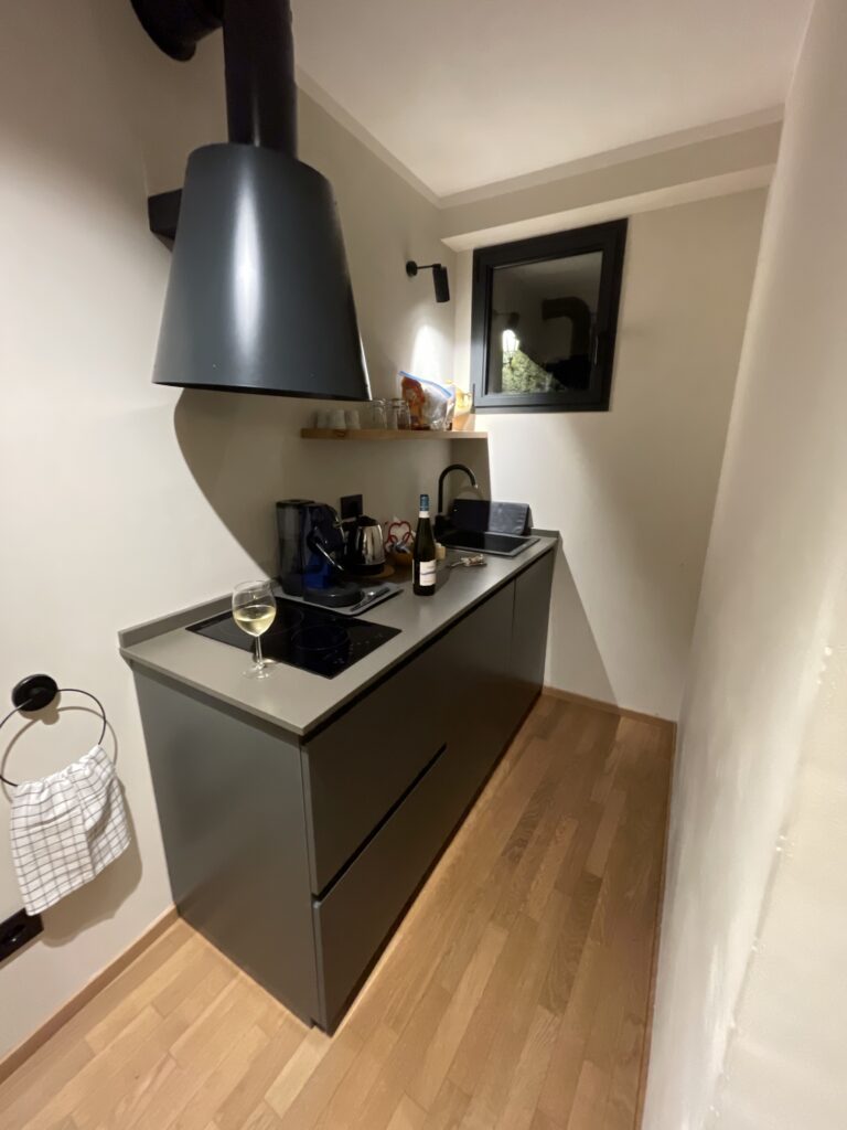 Compact kitchenette at Casa Cicetta with stovetop, sink, coffee machine, and a glass of white wine prepared during a relaxing evening in 2 days in San Marino.