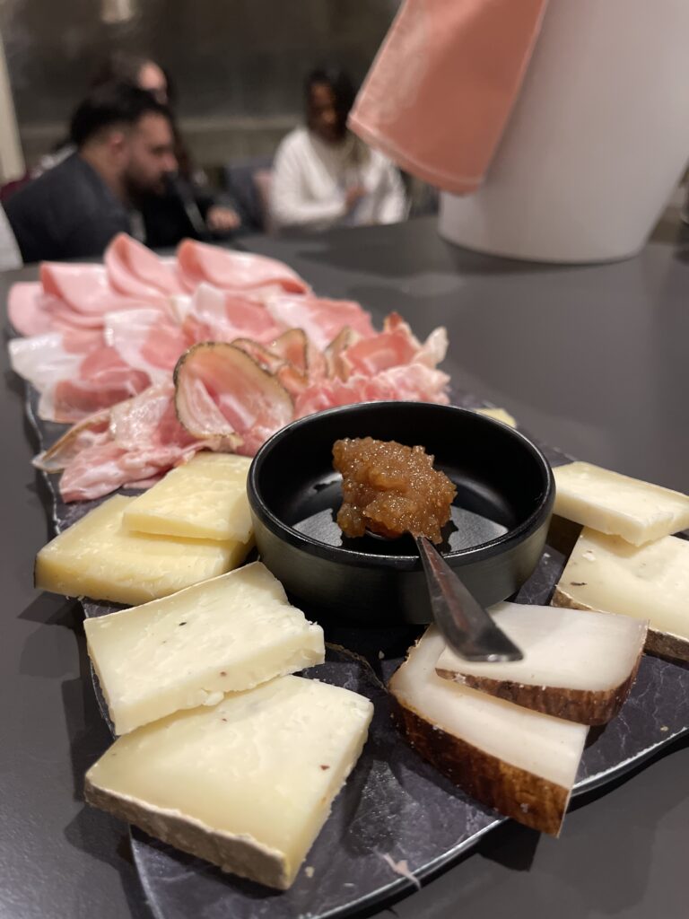 Charcuterie board with slices of cured meats, assorted cheeses, and a small bowl of spread in the center served at a restaurant during 2 days in San Marino.