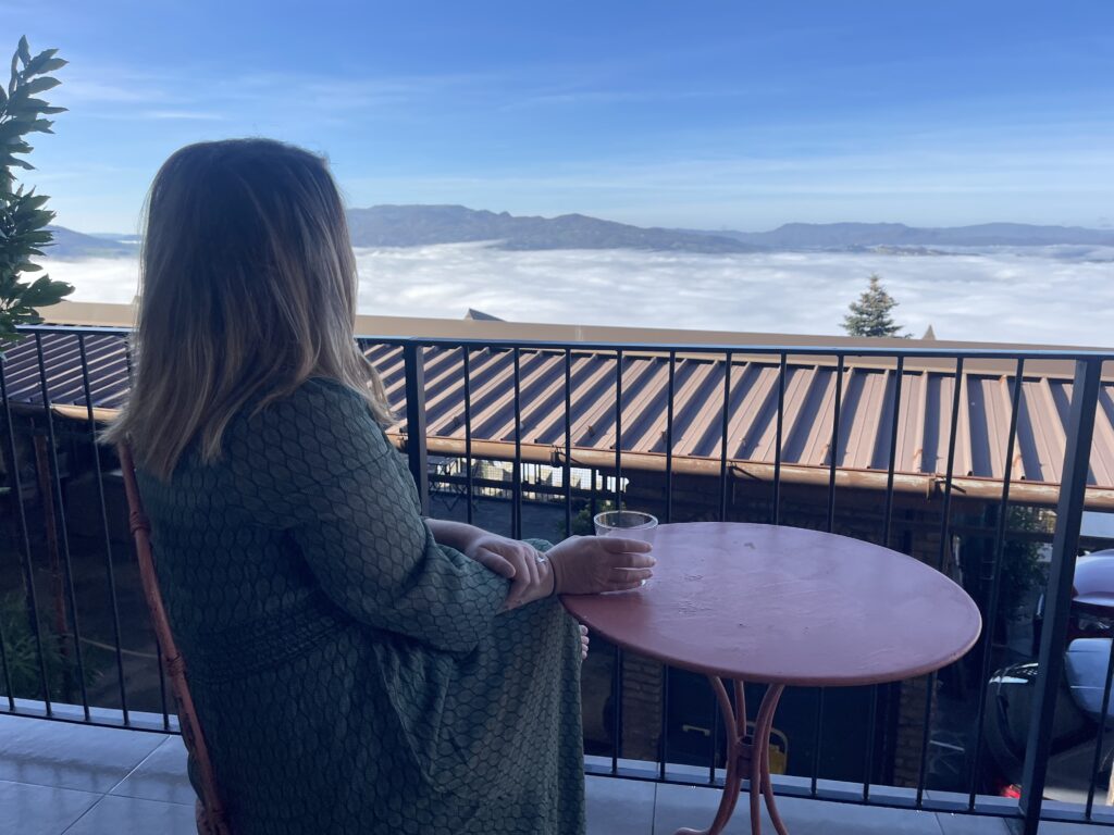 Woman sitting on a balcony at Casa Cicetta overlooking a sea of clouds and distant mountains while holding a drink during 2 days in San Marino.