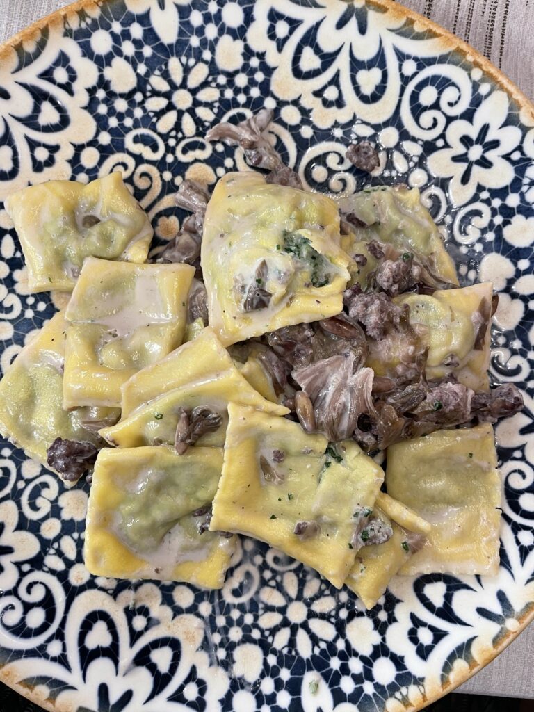 Square stuffed pasta topped with mushrooms and small pieces of meat in a creamy sauce on a decorative plate, a hearty meal during 2 days in San Marino.