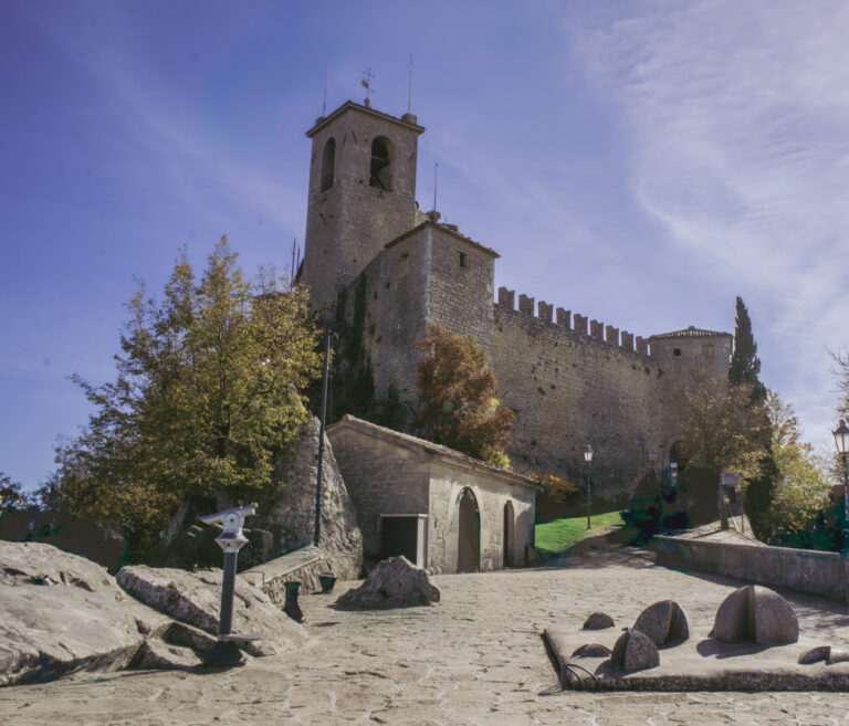 Stone courtyard of Guaita Fortress with crenelated walls, tower, and sunlit pathways surrounded by autumn trees, a historic highlight during 2 days in San Marino.