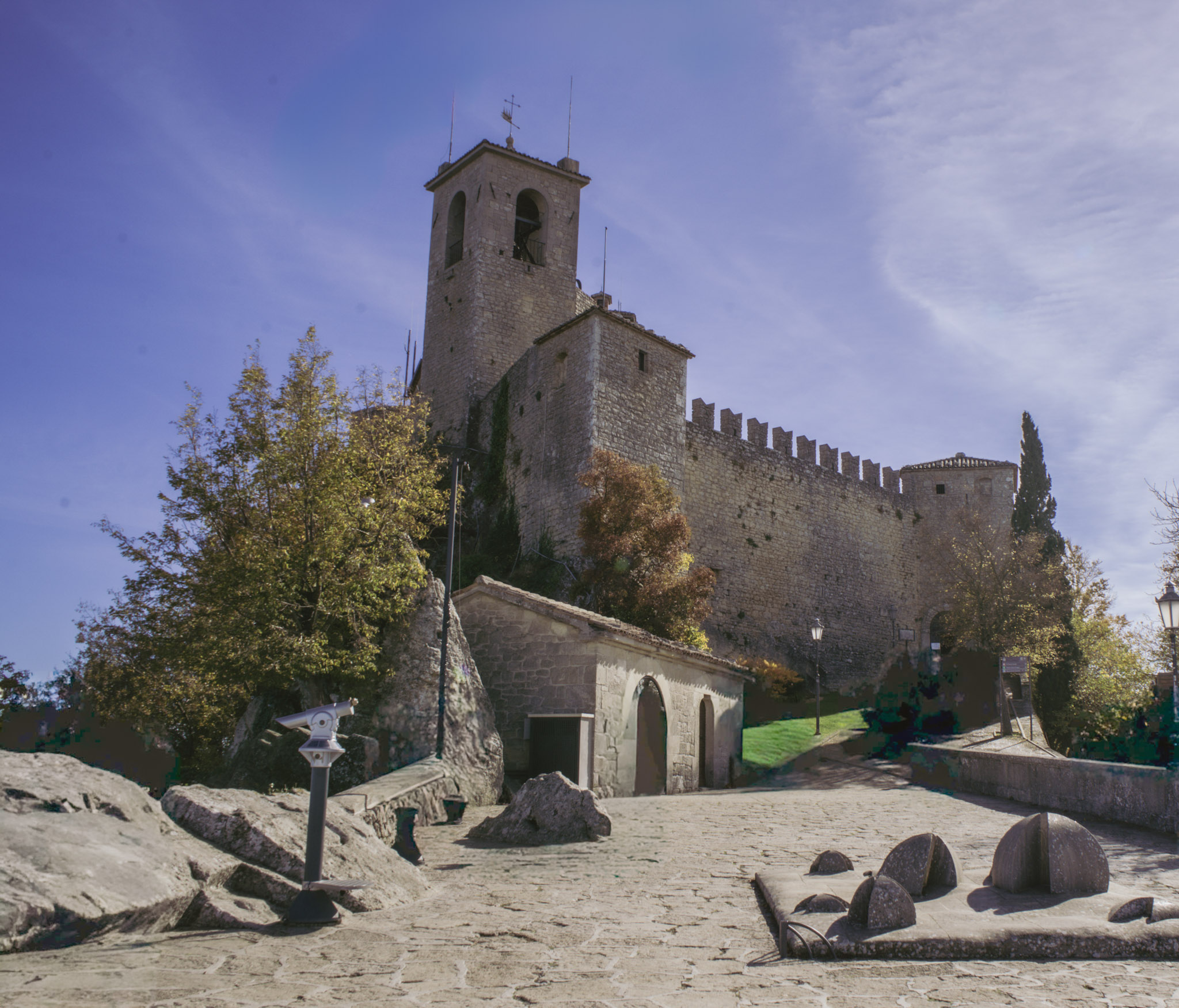 Stone courtyard of Guaita Fortress with crenelated walls, tower, and sunlit pathways surrounded by autumn trees, a historic highlight during 2 days in San Marino.