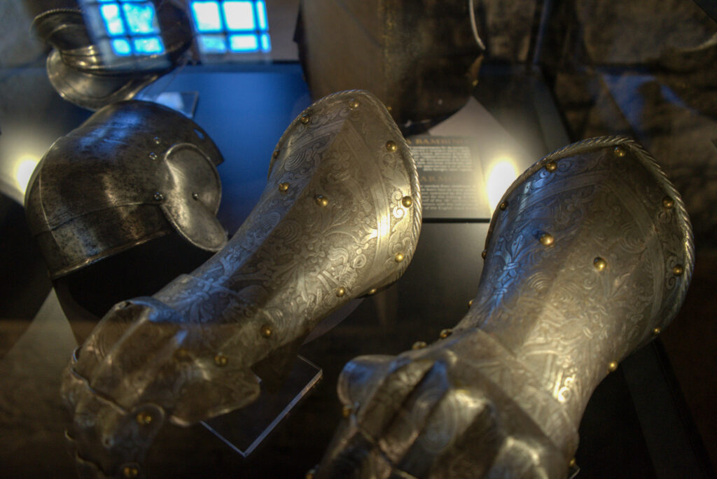 Ornate engraved metal gauntlets and a helmet displayed in a museum case with soft lighting, showcasing historic armor seen during 2 days in San Marino.