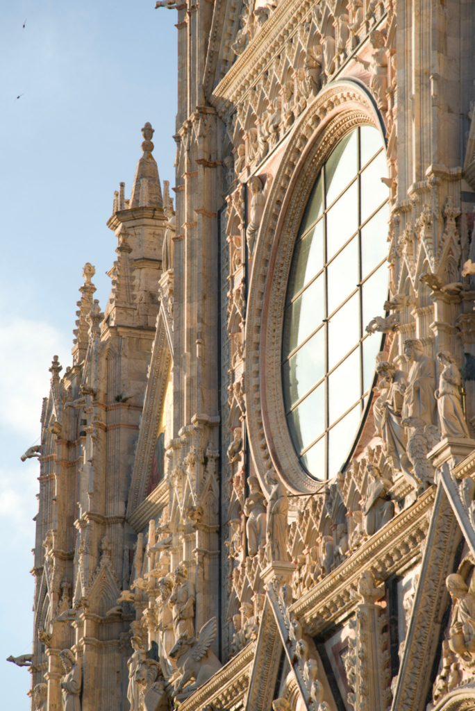 Close detail of the Siena Duomo rose window surrounded by carved sculptures of saints, angels, and Gothic spires.