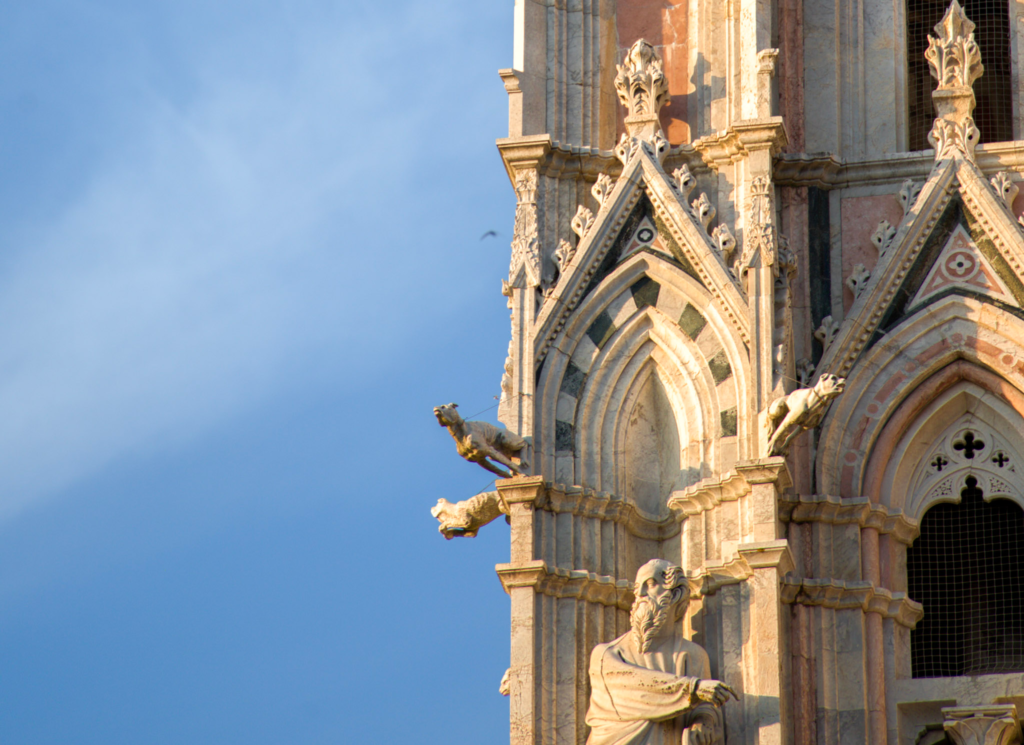 Cluster of sculpted saints, a winged lion, and a winged ox on the upper facade of the Siena Duomo, gilded by late afternoon sun.