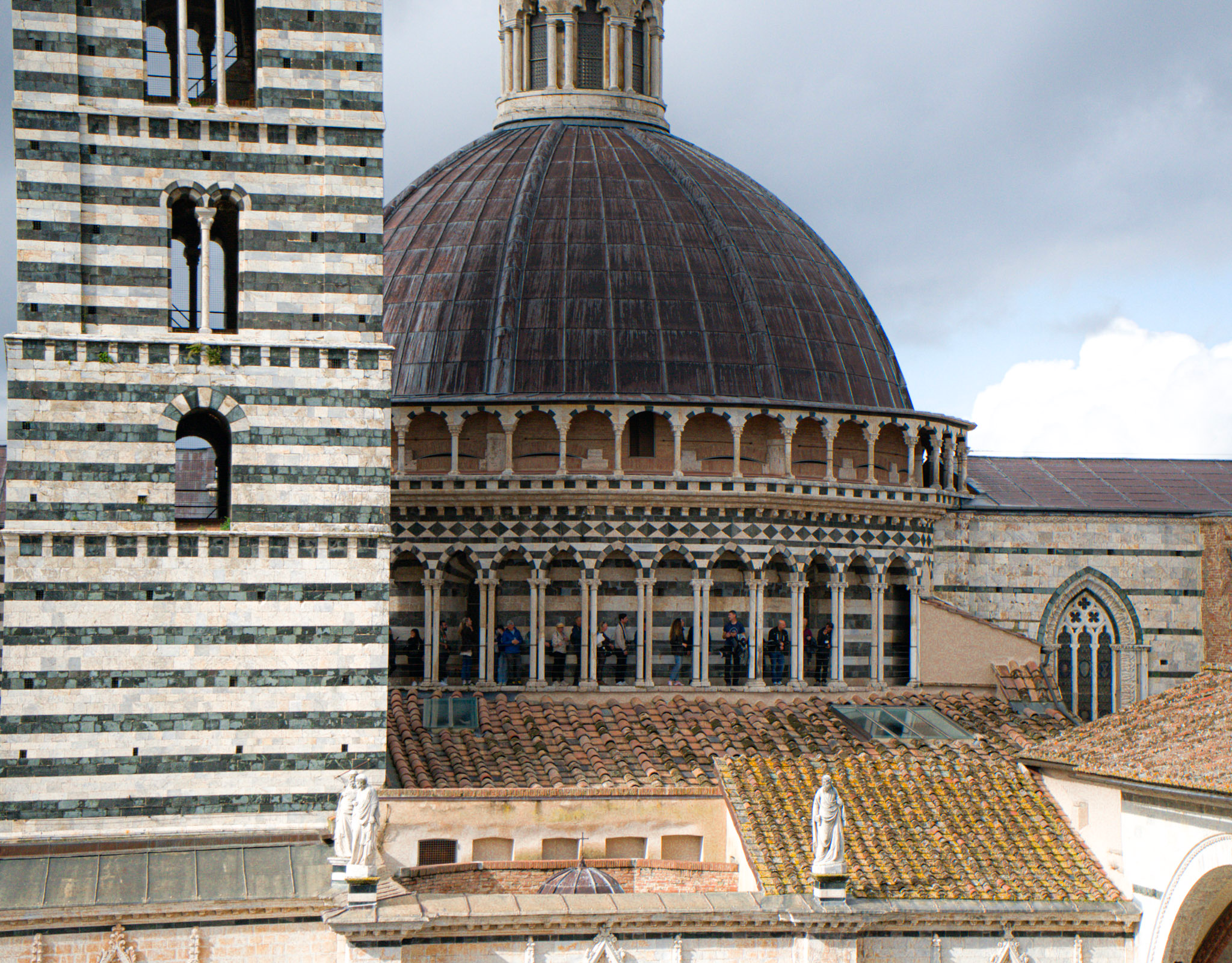 lose view of the Siena Duomo dome and striped bell tower with a row of arches where visitors stand looking out over the city. This perspective highlights the architectural detail you can experience during a Siena Duomo visit on a 2 days in Siena itinerary.