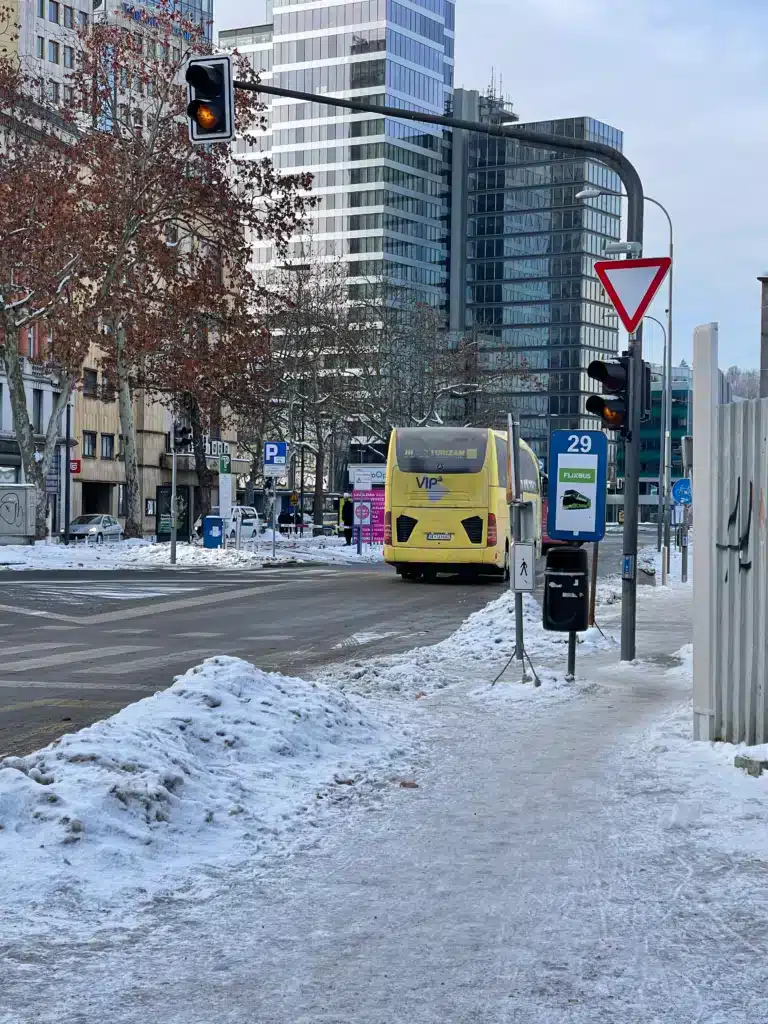 Ljubljana bus station Flixbus boarding slot 29 in winter with snow on sidewalks and a yellow tour bus