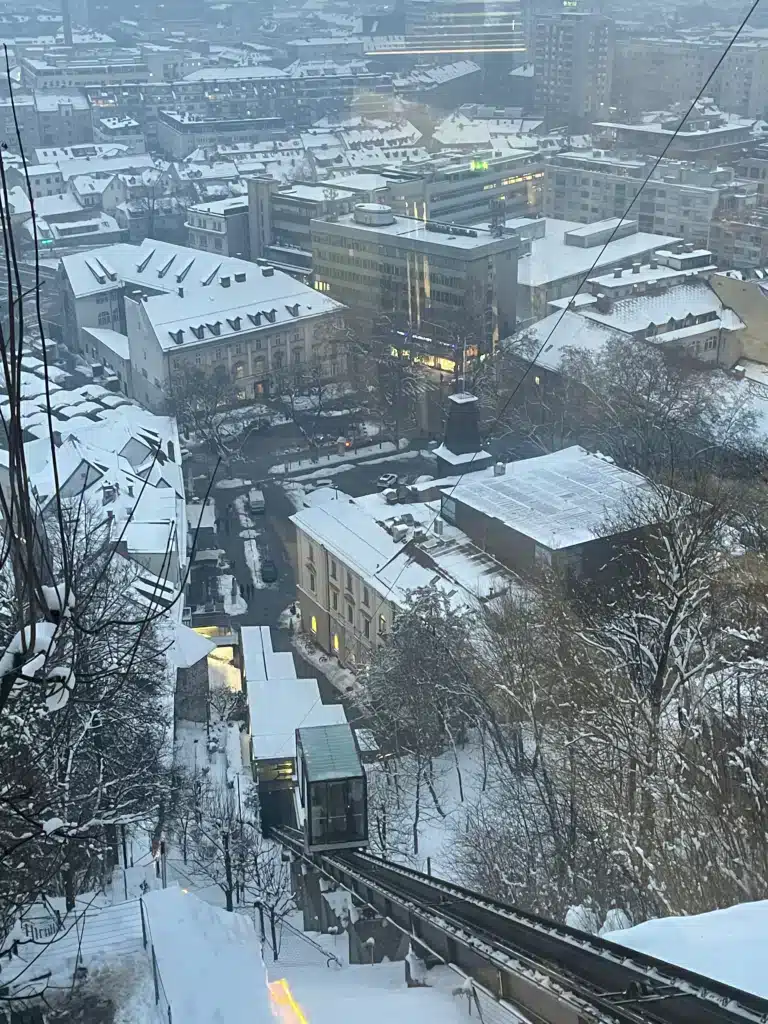 View from Ljubljana Castle funicular descending over snow-covered old town buildings in winter
