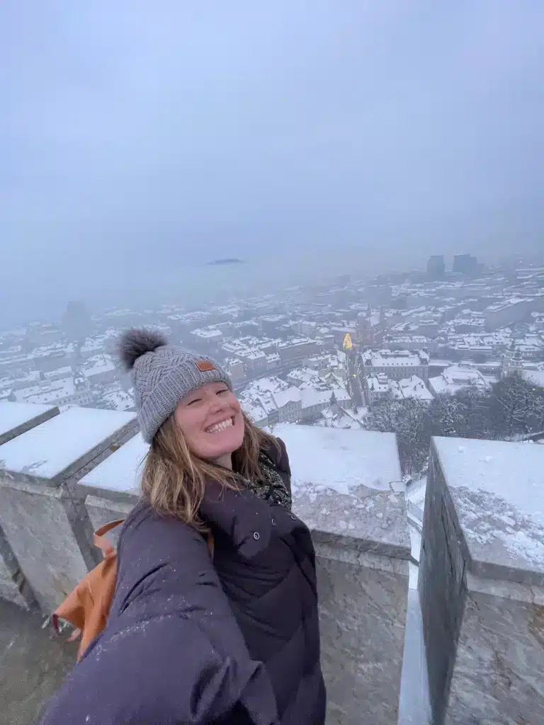Solo female traveler at Ljubljana Castle viewpoint in winter overlooking snow-covered Ljubljana old town