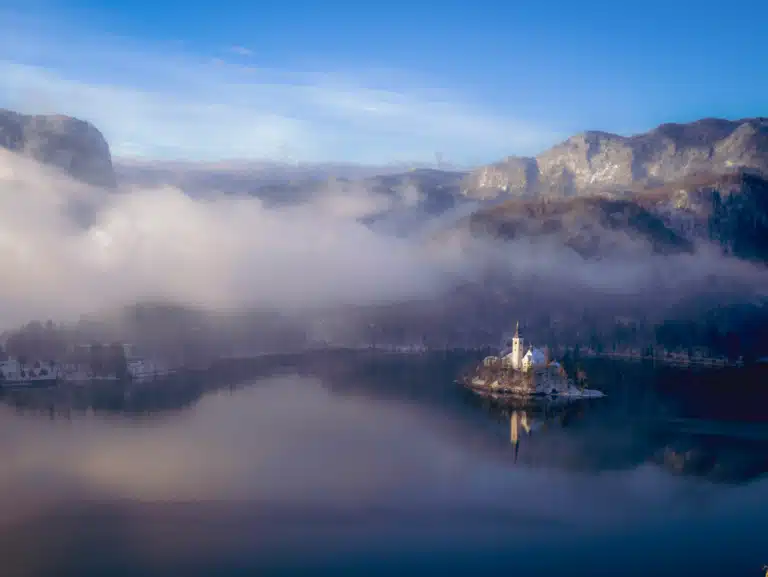 Lake Bled at dawn in January with mist over the Julian Alps and the Church of the Assumption reflected in still water