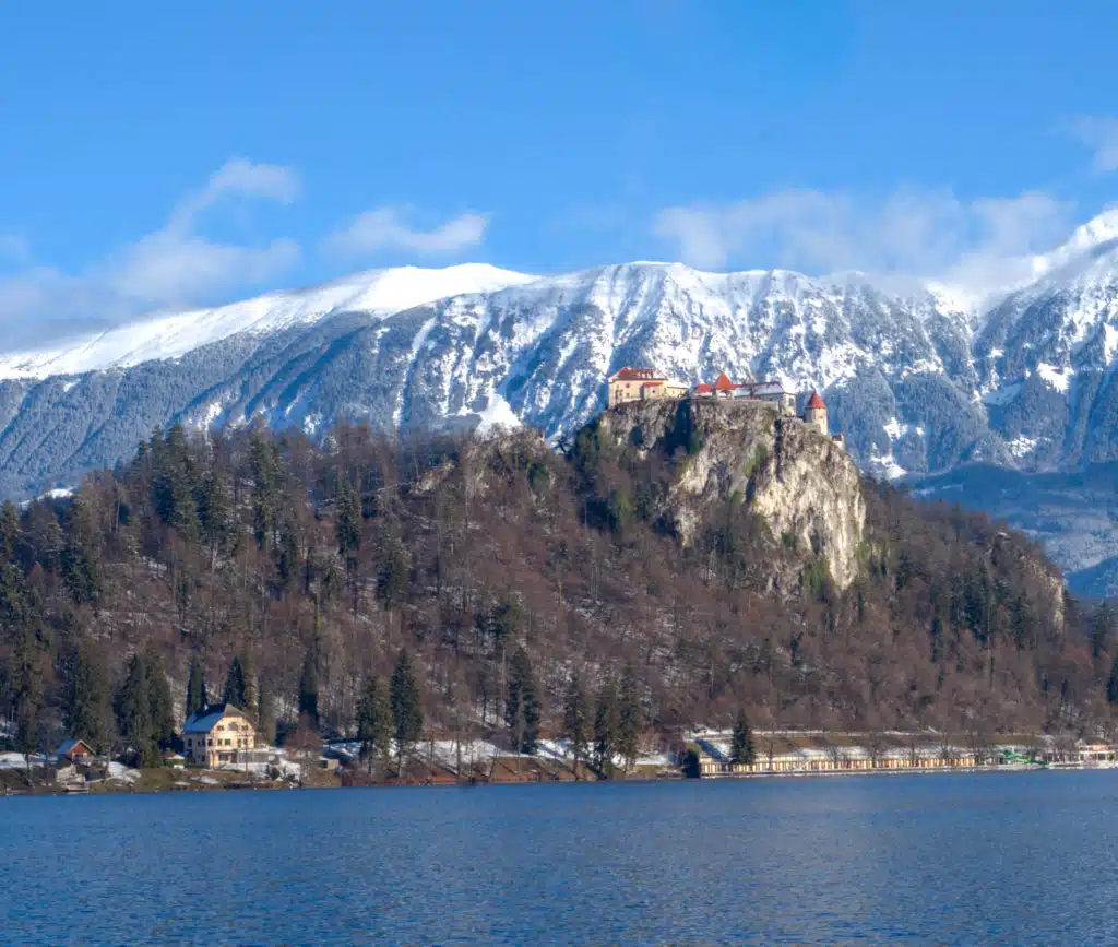 Lake Bled Castle perched on cliff above the lake in winter with snow-covered Julian Alps in the background