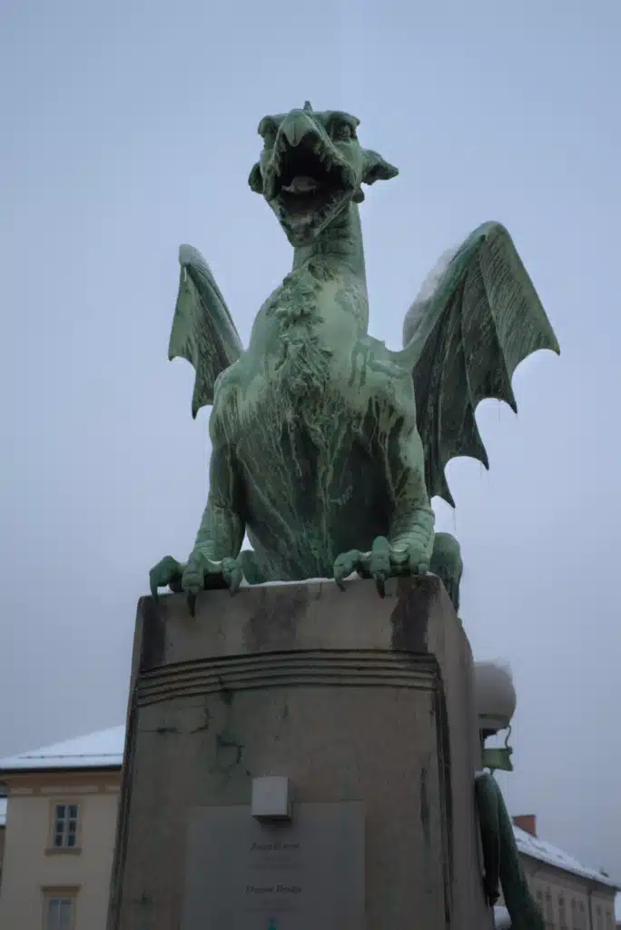 Green copper dragon statue on Dragon Bridge (Zmajski Most) in Ljubljana with snow on its wings in winter