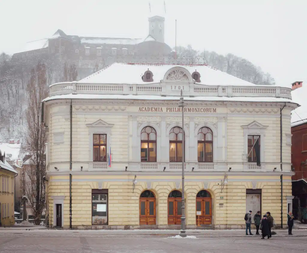 Slovenian Philharmonic Hall in Ljubljana with Academia Philharmonicorum inscription and Ljubljana Castle on the hill in winter snow