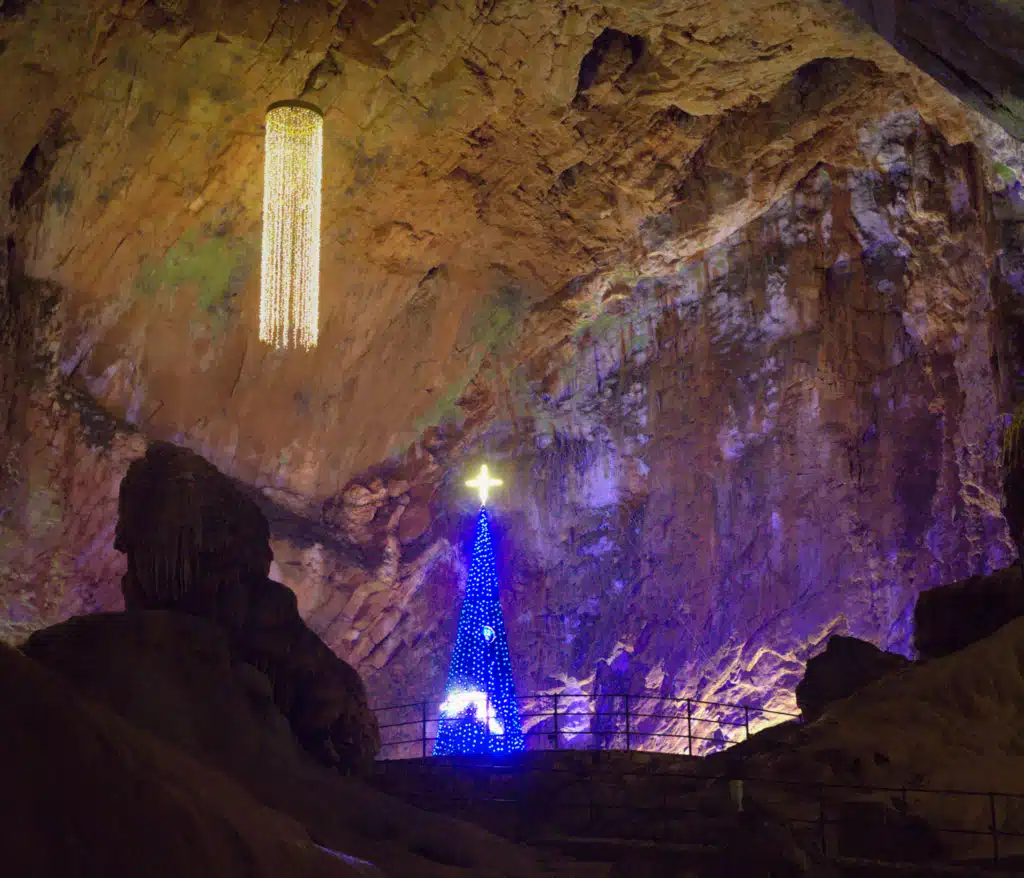 Christmas decorations inside Postojna Cave in Slovenia with a hanging chandelier and lit blue Christmas tree in a cave chamber