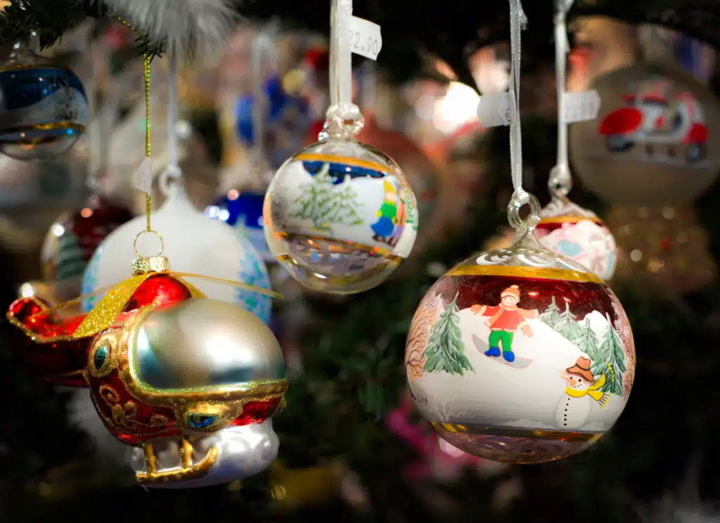 Hand-painted Lissy glass Christmas baubles with winter scenes hanging at a Bruneck market stall, price tags visible